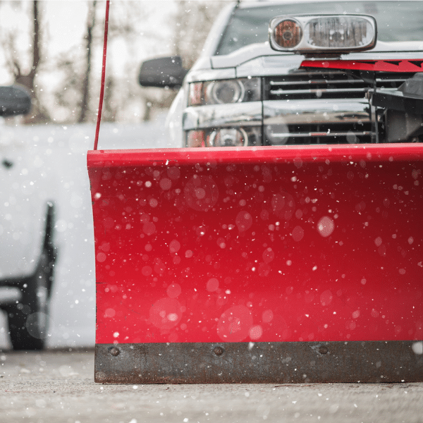 Snow plow clearing large warehouse lot during sunrise in Utah